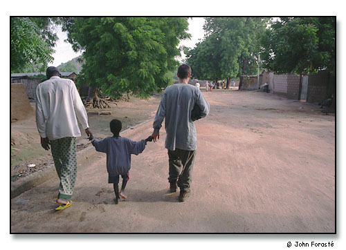 André Doucha, his youngest son and Alex Forasté (Peace Corps Volunteer) visiting as they stroll through their town. <br>Mora, Cameroon, (central west) Africa. August 2002.